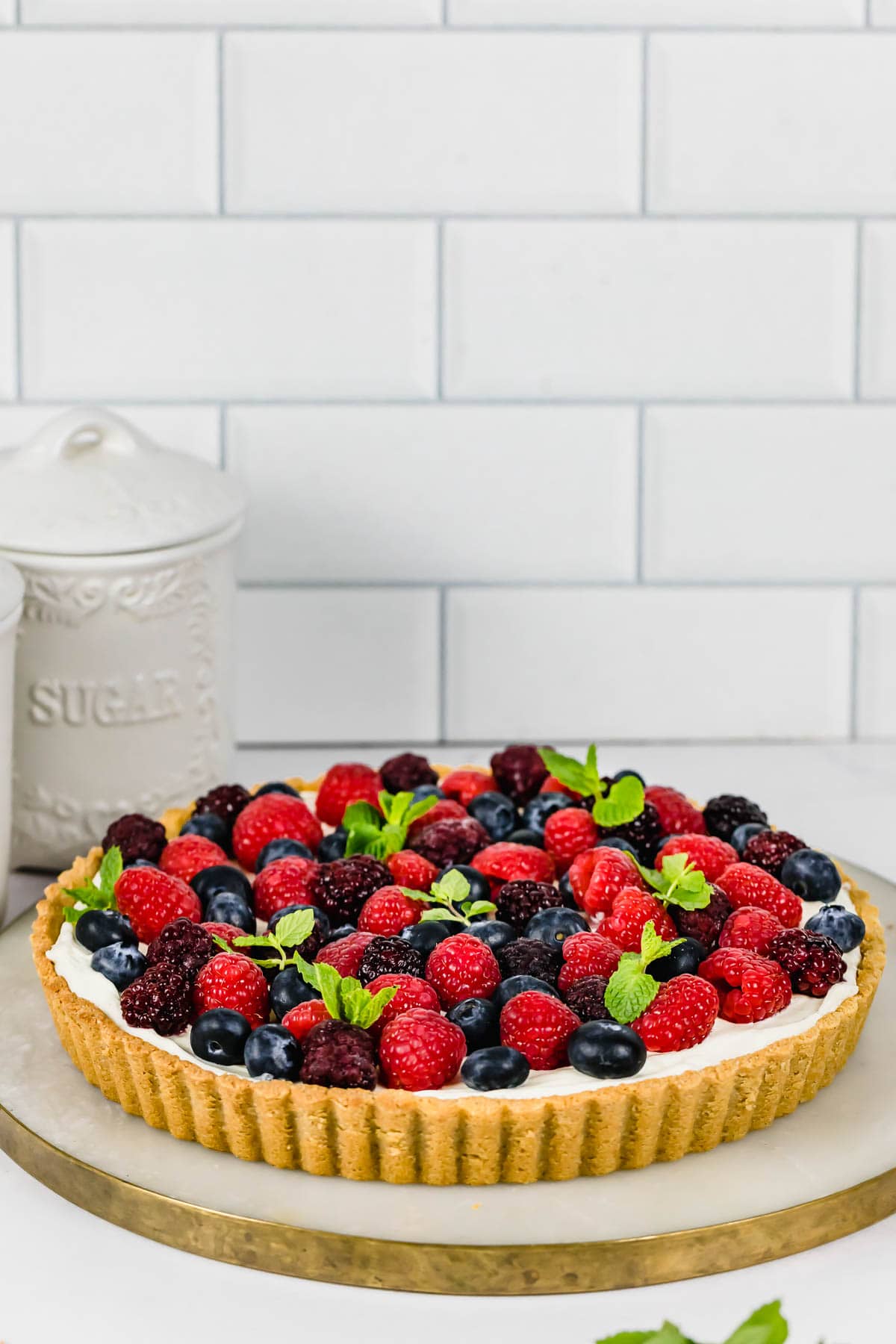 A mixed berry tart sitting on a marble cutting board on a kitchen counter.