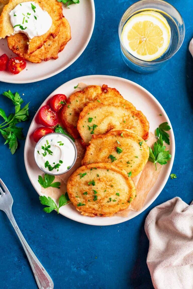 A plate of potato pancakes served with sour cream and fresh tomatoes.
