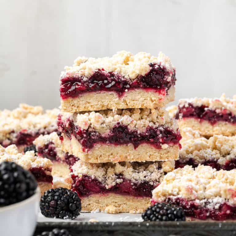 A stack of three blackberry pie bars sitting on a baking sheet.