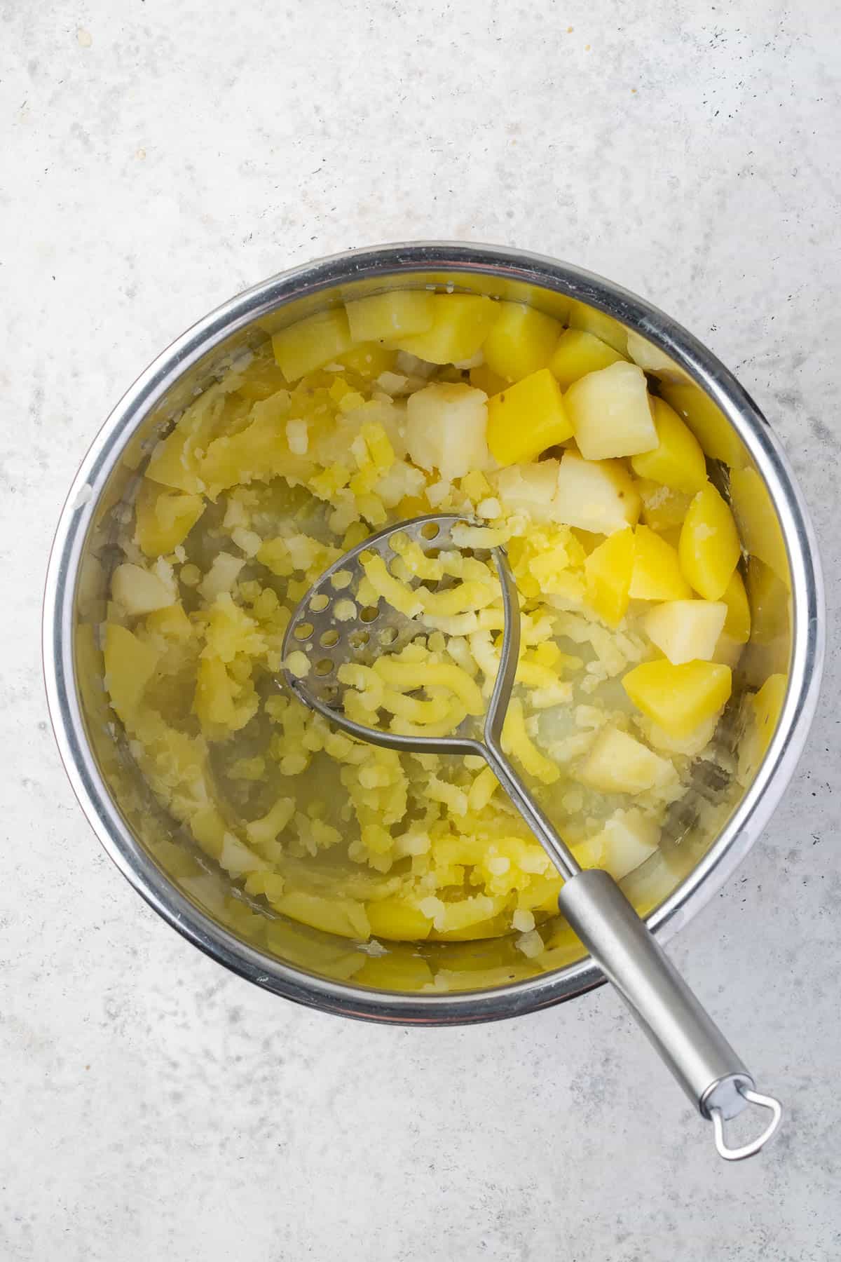 Cooked potatoes being mashed with a potato ricer. 