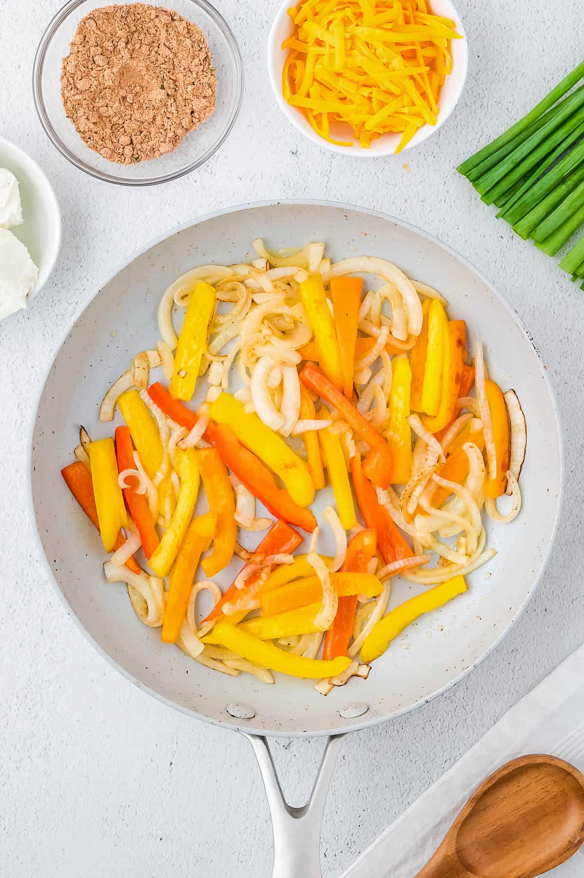 Sliced bell peppers and onions cooking in a large skillet. 