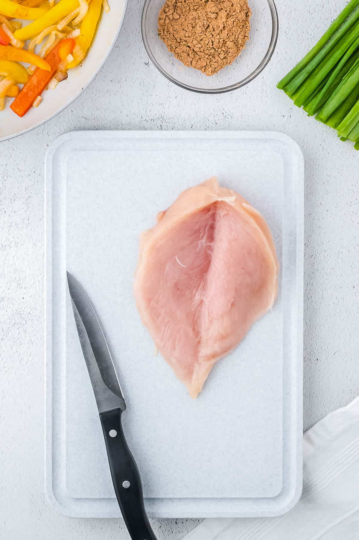 A chicken breast cut in butterfly fashion laying on a cutting board.