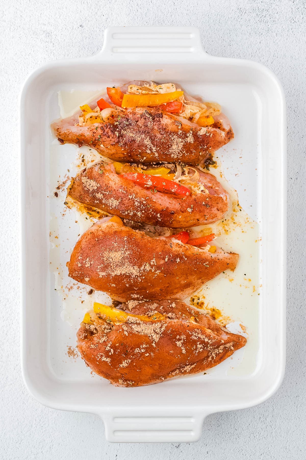 Four fajita stuffed chicken breasts in a ceramic baking dish. 