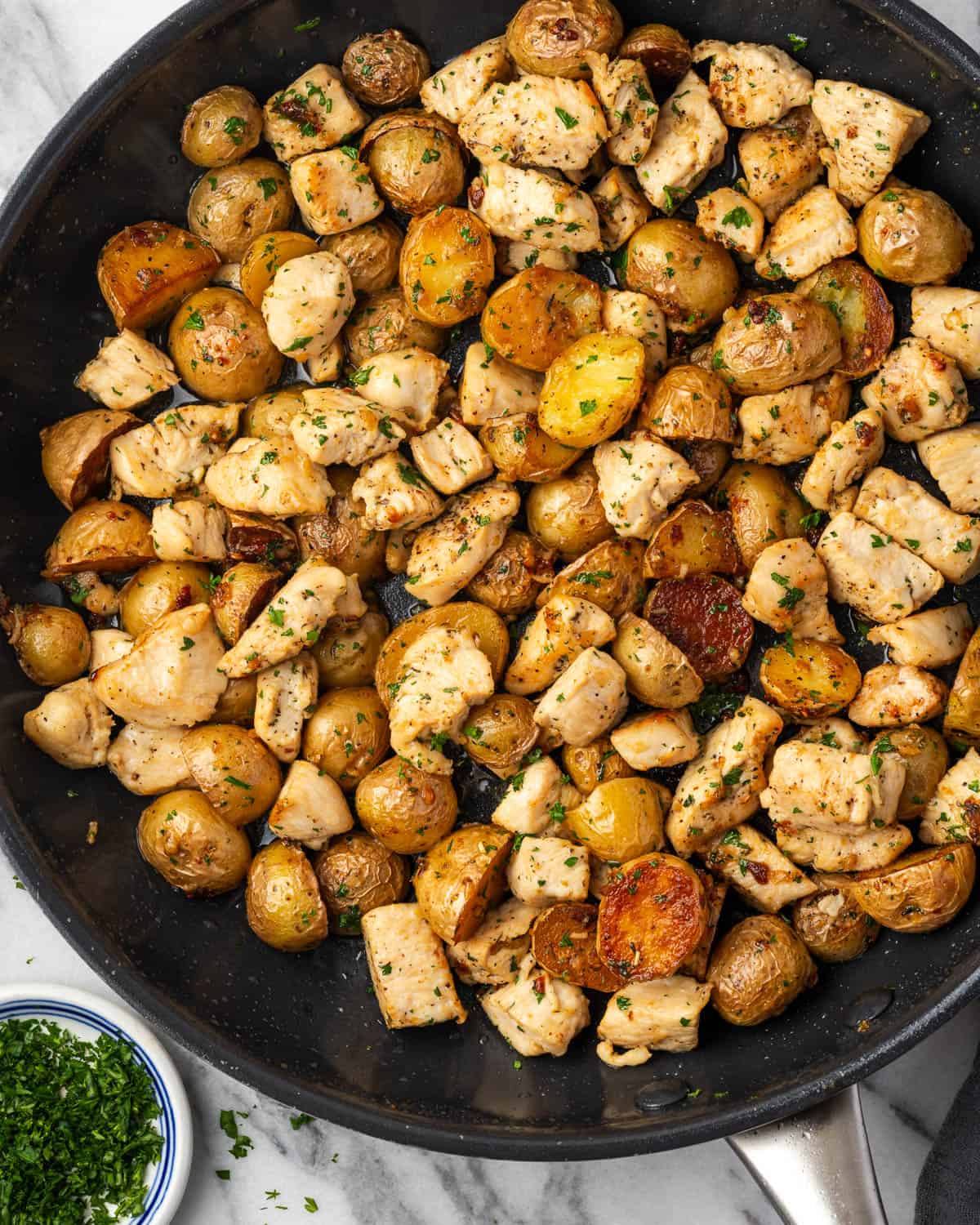 A large skillet filled with chicken and potatoes in a garlic butter sauce.