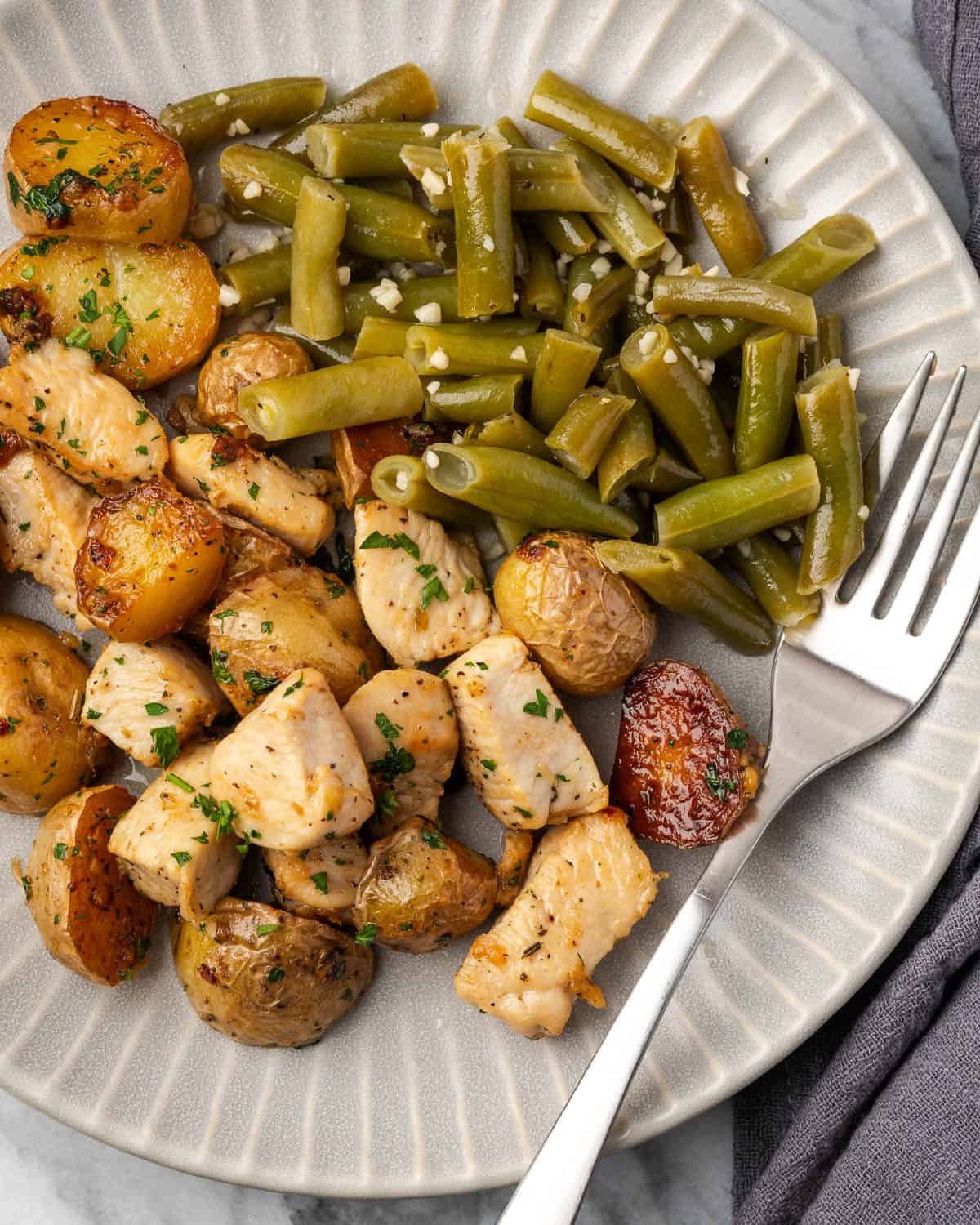 A serving plate with garlic butter chicken and potatoes and a side of green beans. 