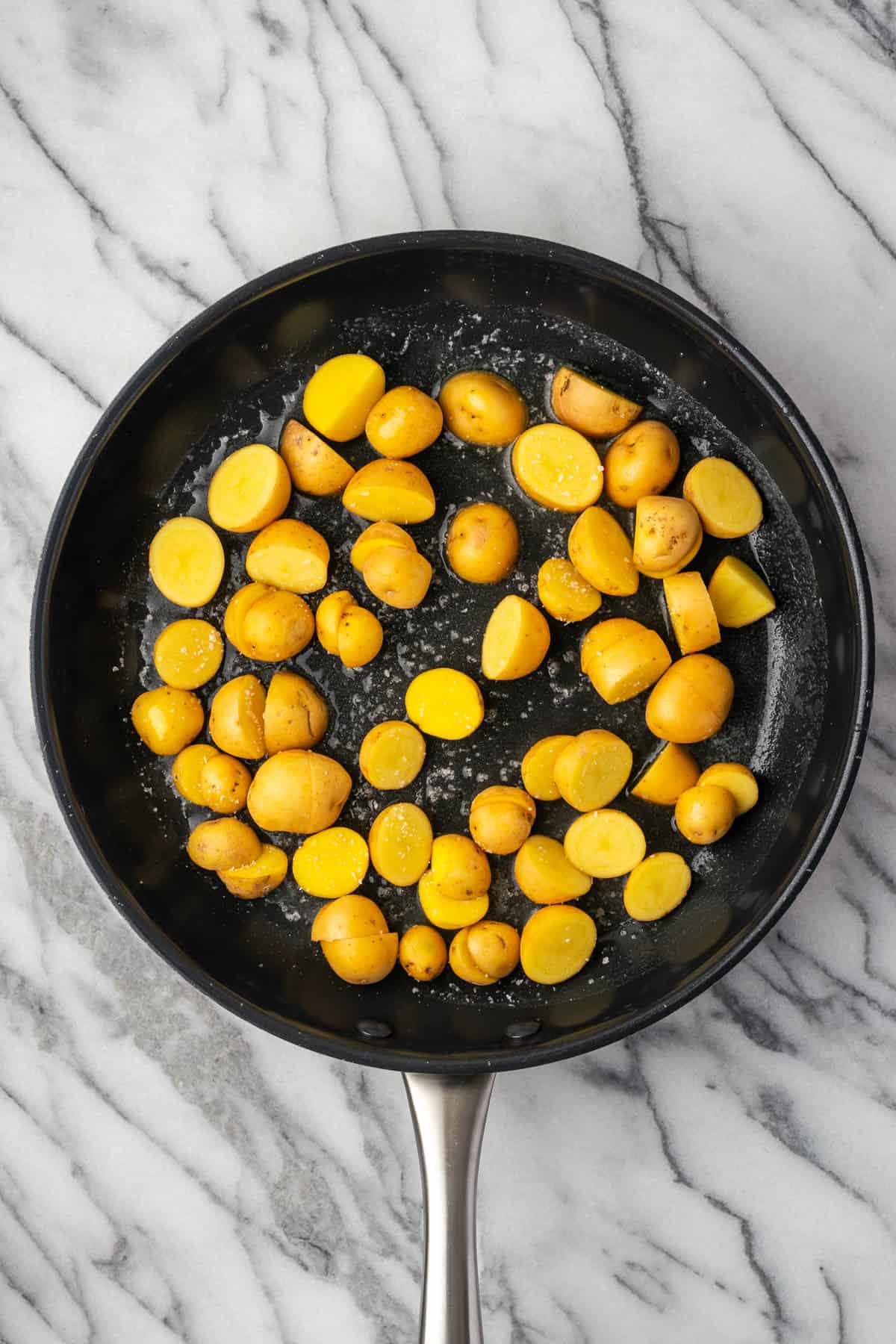 Salted potatoes being sauteed in a large skillet.