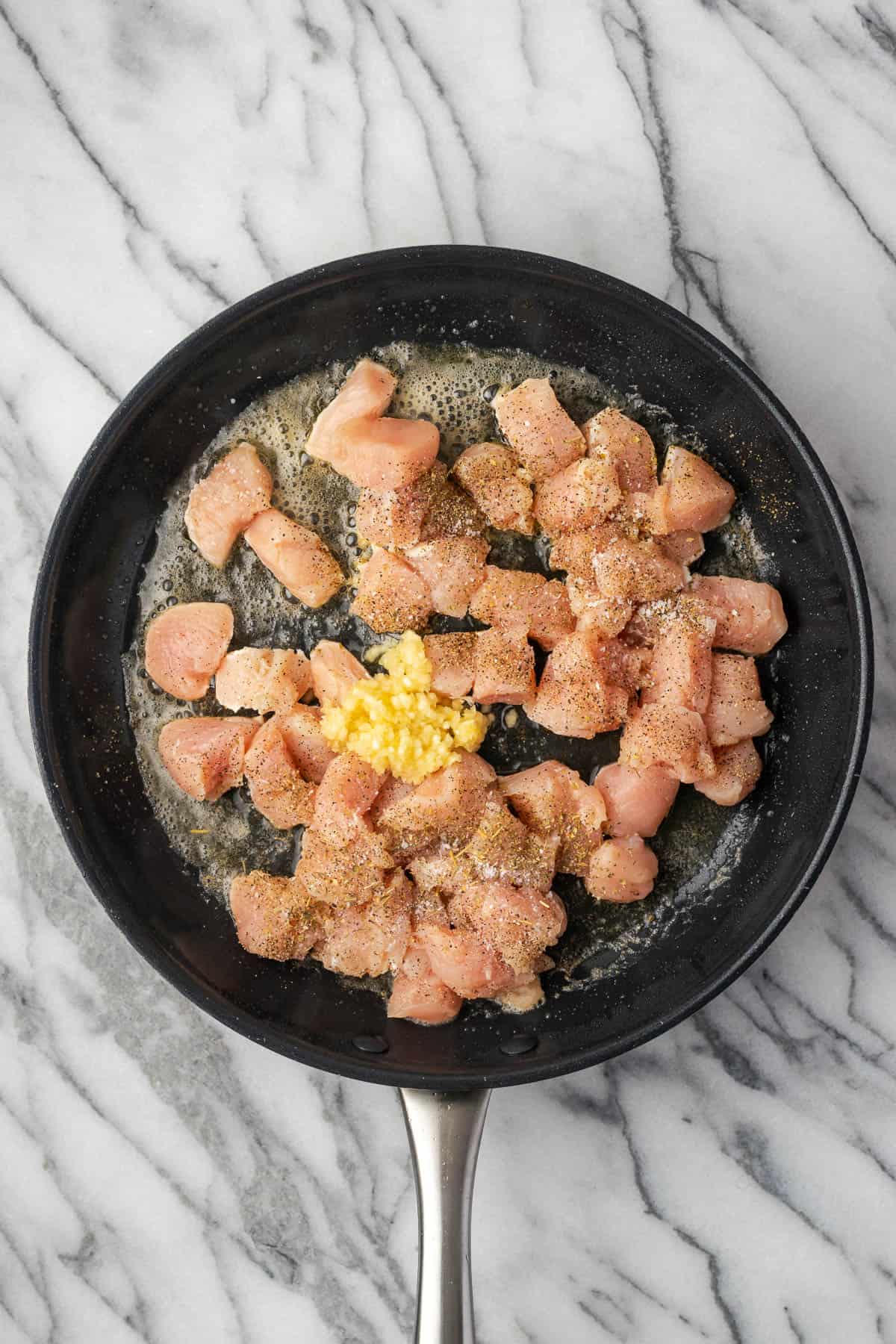 Chicken pieces cooking in a large skillet.