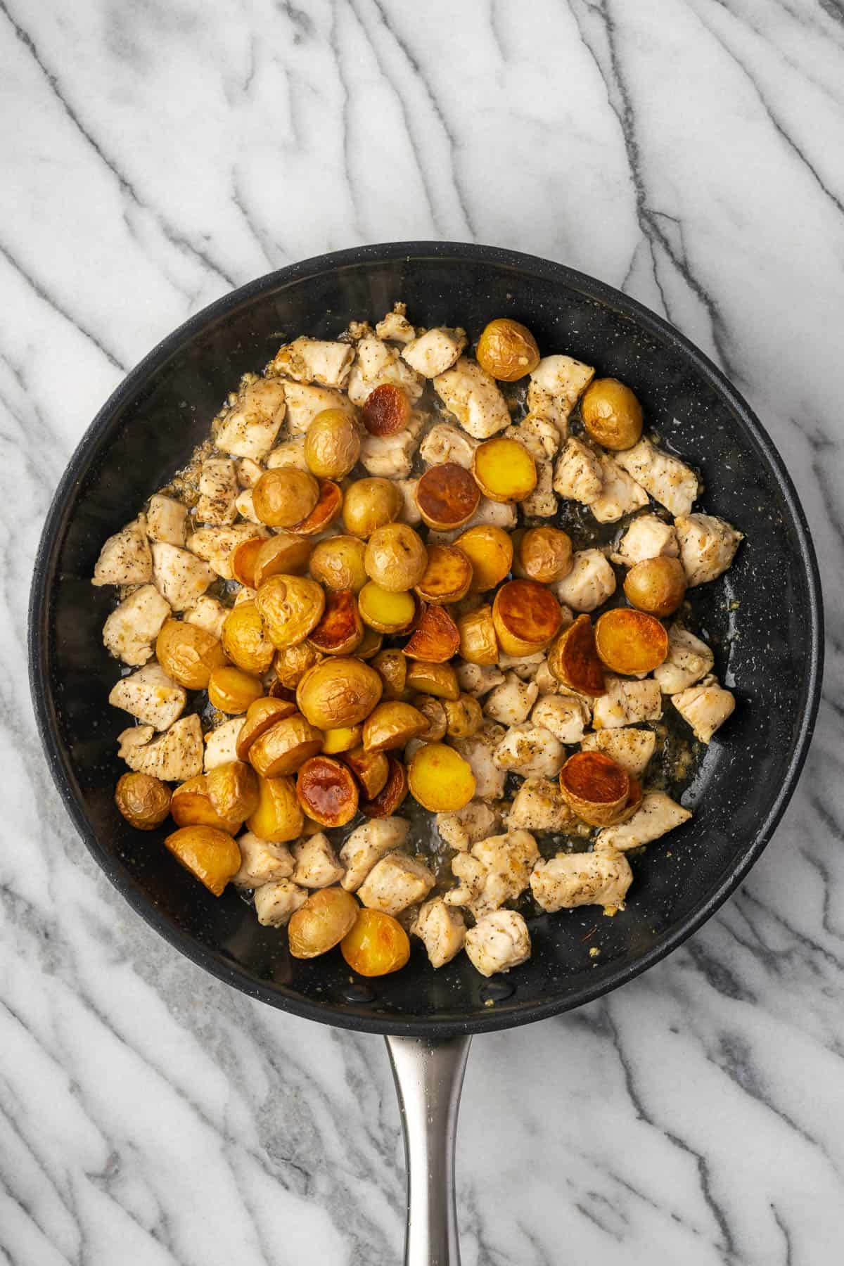Cooked potatoes being returned to the pan with the chicken. 
