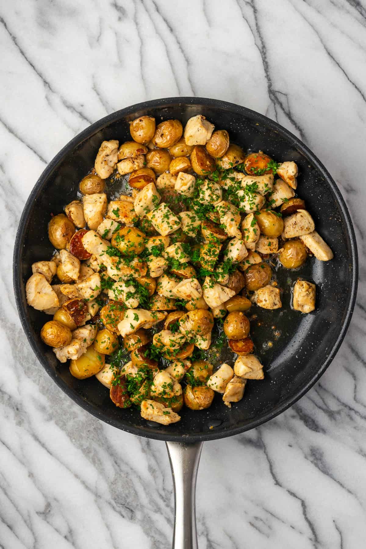 Fresh parsley being added into the pan with the garlic butter chicken and potatoes.