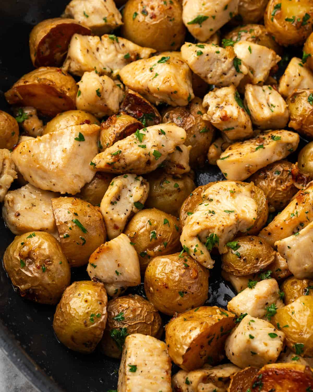 A pan of cooked chicken and potatoes covered with garlic butter and parsley.