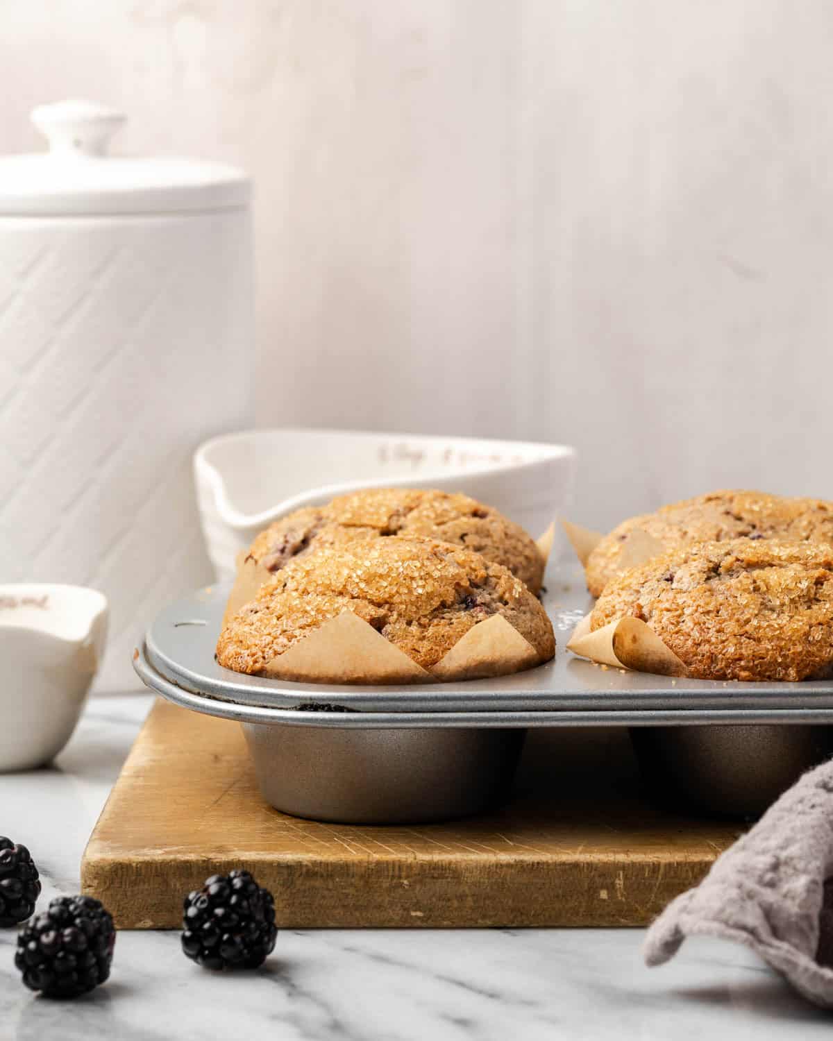Freshly baked gluten free blackberry muffins in a muffin tin sitting on a marble counter.