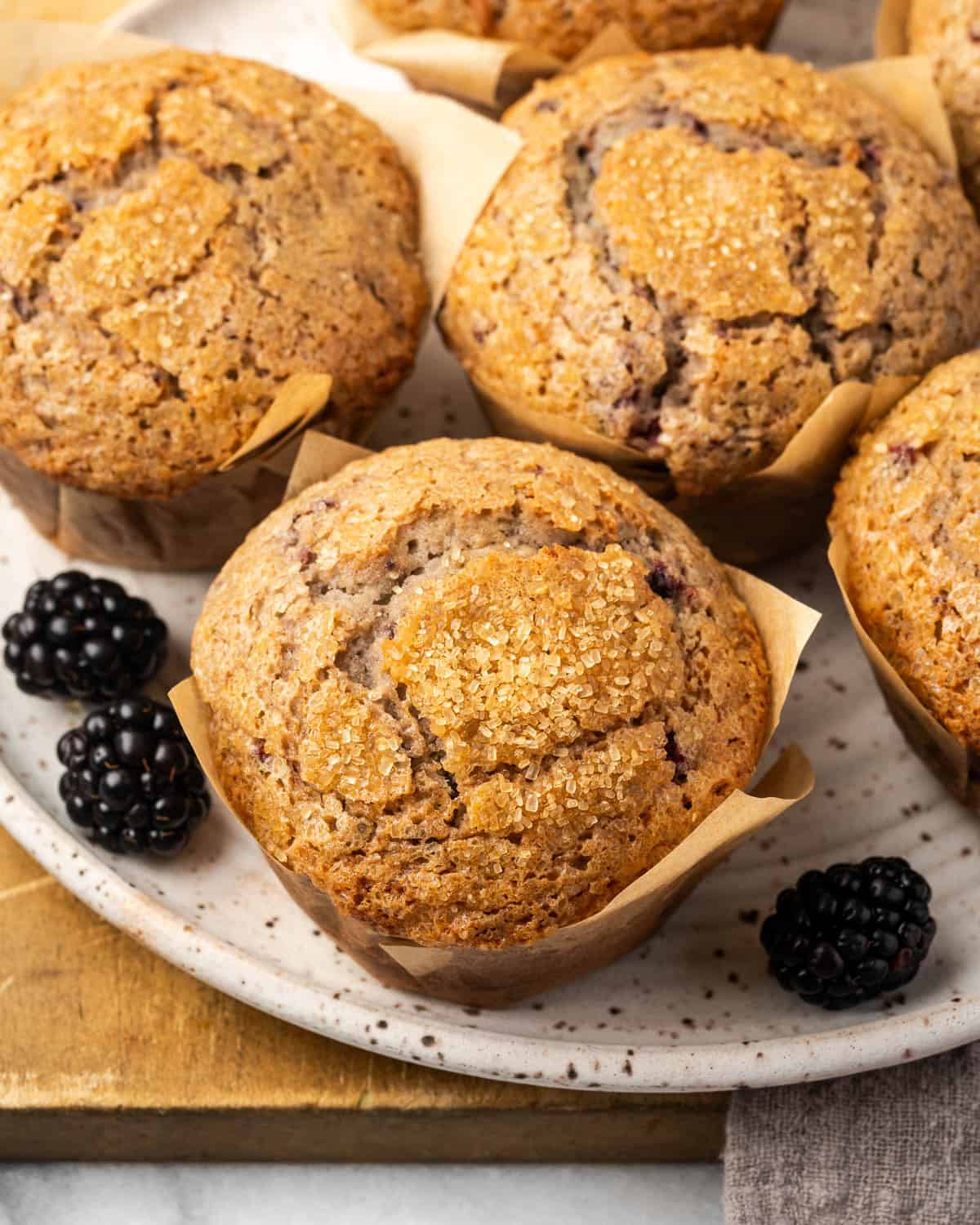 A batch of blackberry muffins sitting on a serving plate alongside a few fresh berries. 