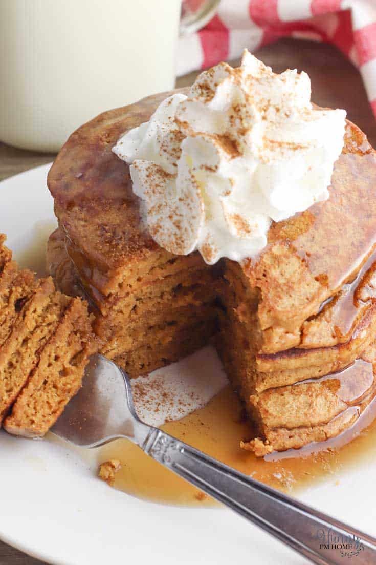 A stack of gluten free gingerbread pancakes topped with whipped cream and a sprinkle of cinnamon. 