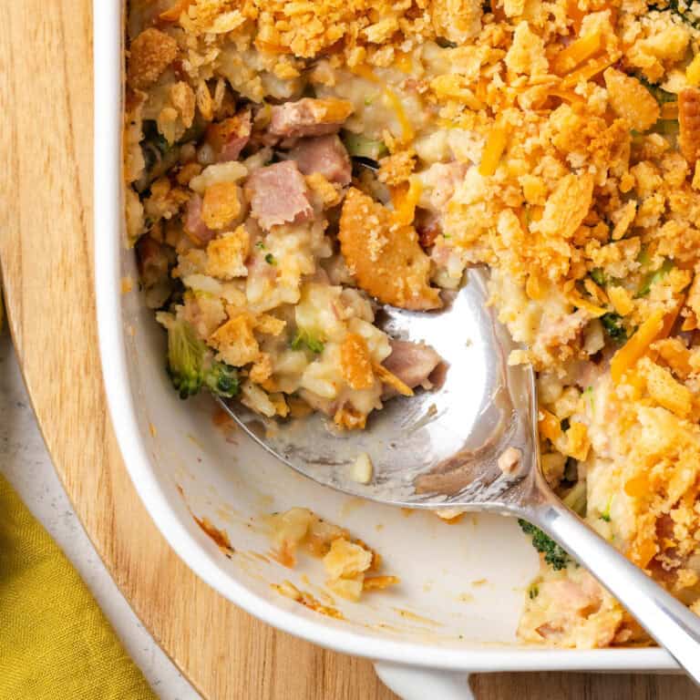 A serving spoon scooping up some ham broccoli rice casserole from a baking dish.