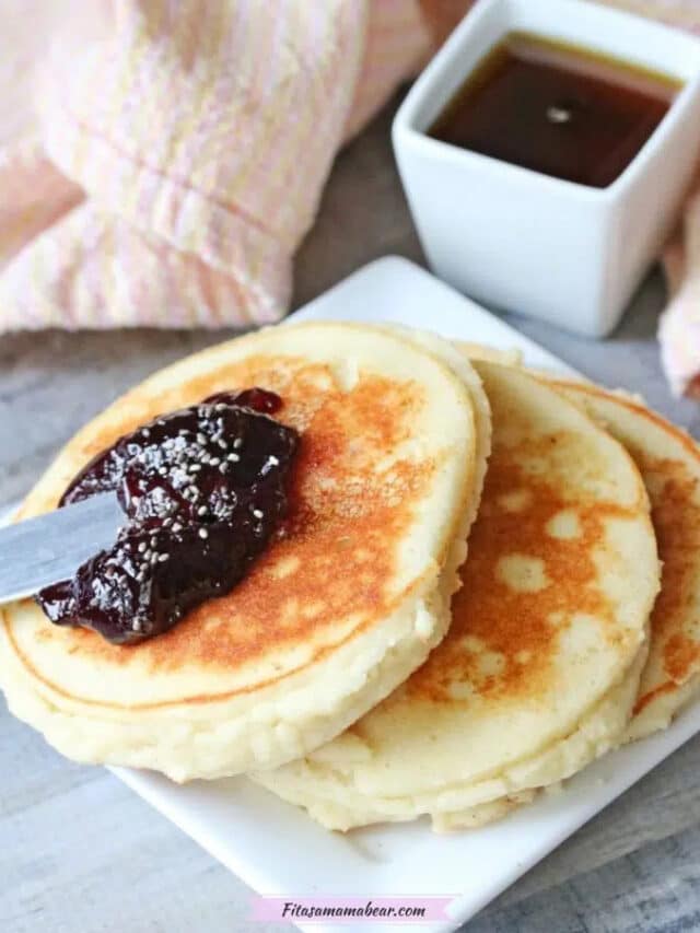 Two high protein yogurt pancakes on a small plate being topped with jam. 