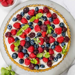 A creamy tart covered with fresh berries sitting on a marble tray.