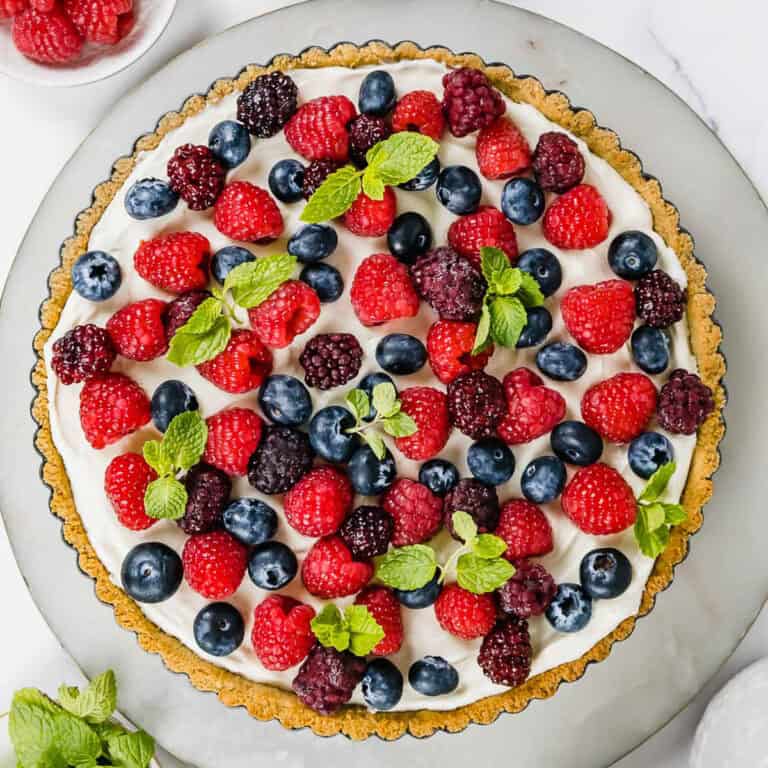 A creamy tart covered with fresh berries sitting on a marble tray.