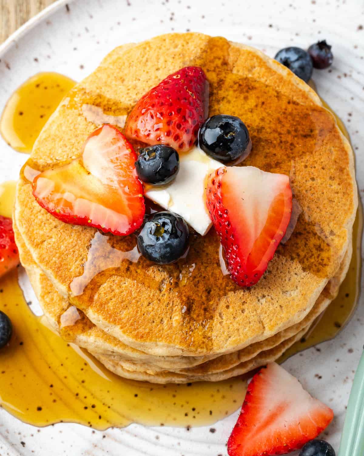 A stack of oat flour waffles topped with fresh berries, butter and maple syrup.