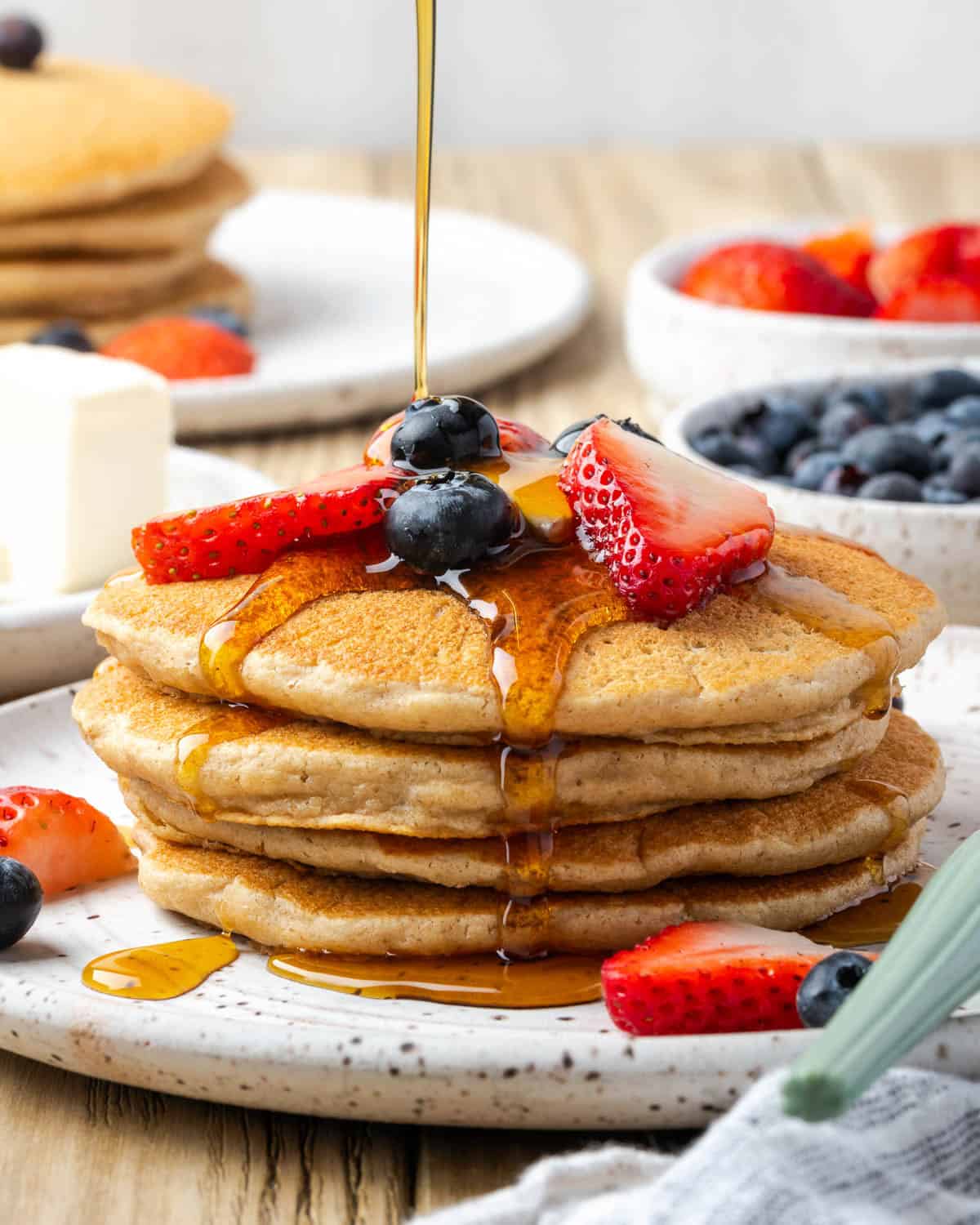 Syrup being poured over a stack of oat flour pancakes on a plate.