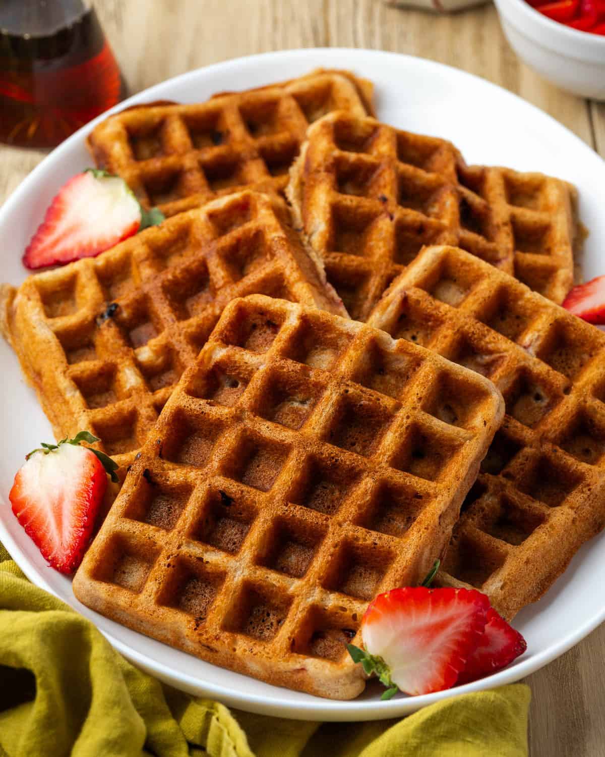 A large platter of gluten free strawberry waffles sitting on a breakfast table. 