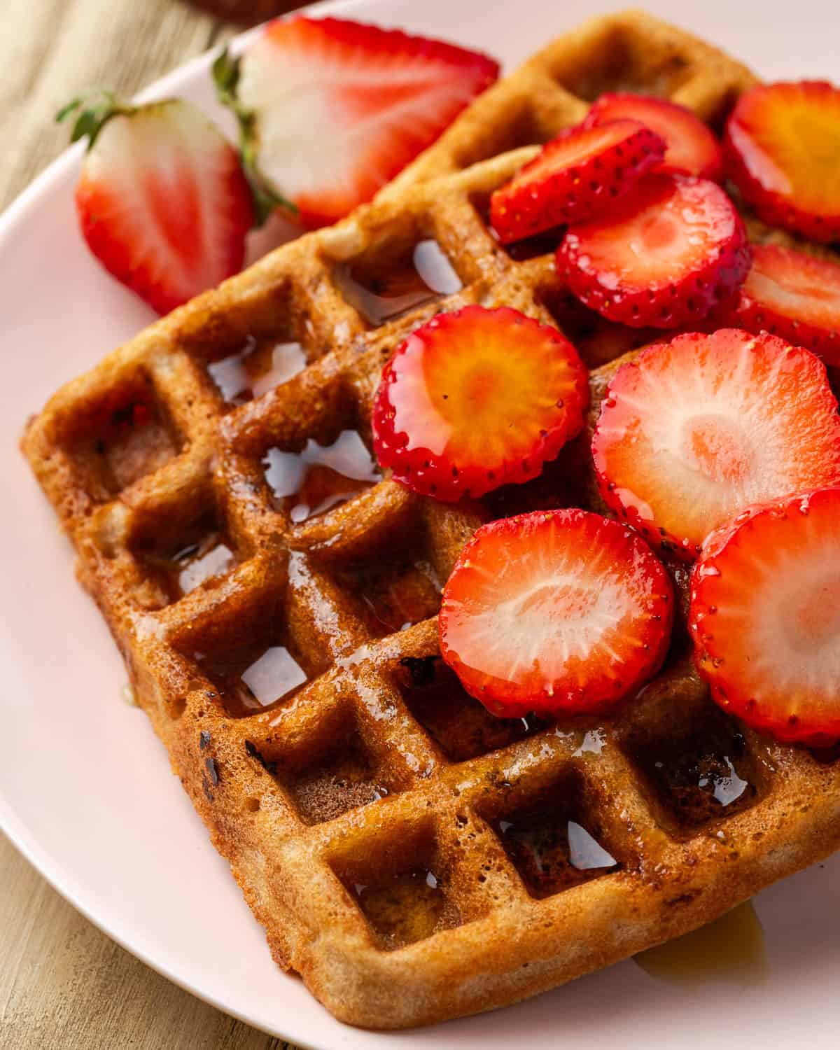 Strawberry waffles served with slices of fresh strawberries and syrup on a small plate.