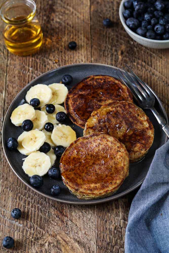 Three vegan protein pancakes served on a plate with a side of fresh fruit. 