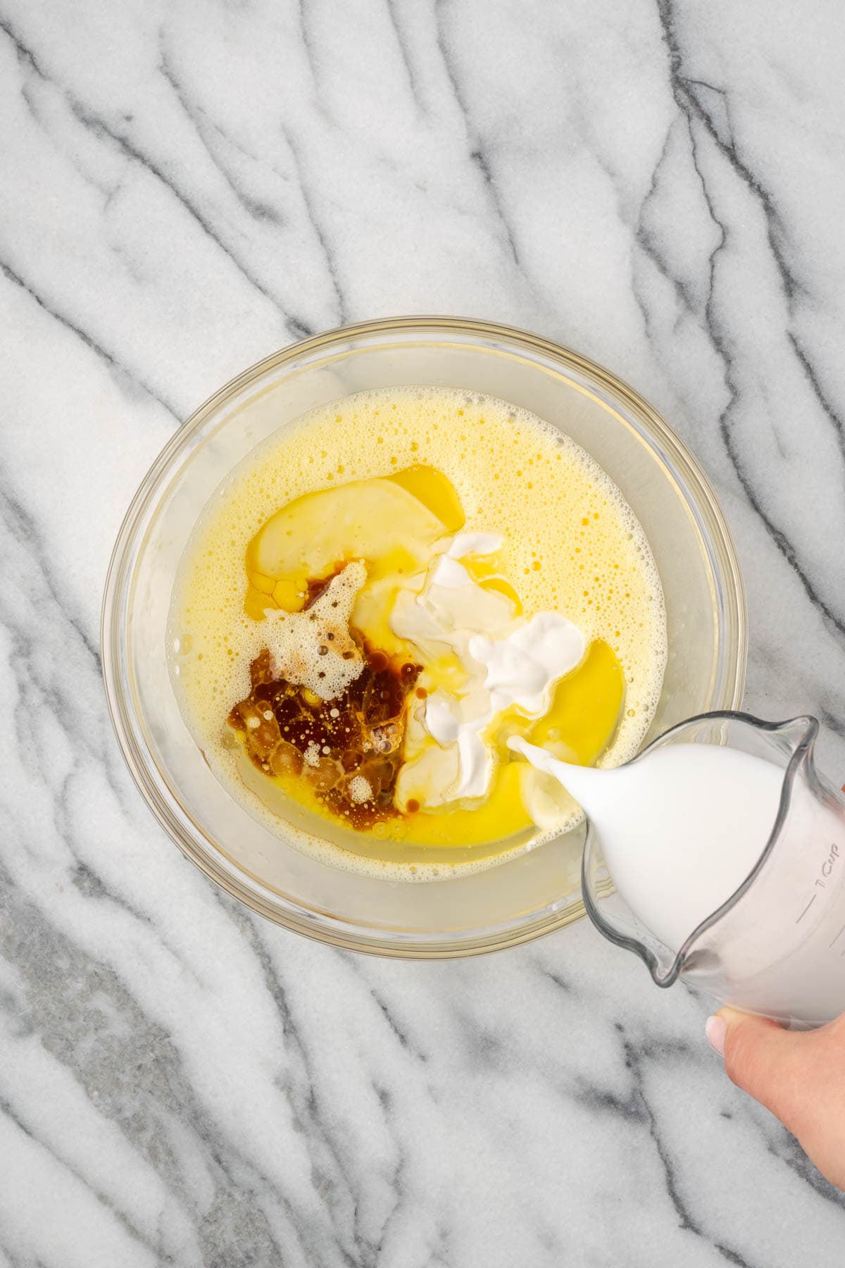 Sour cream, milk, oil and vanilla being mixed into the bowl with the beaten eggs. 