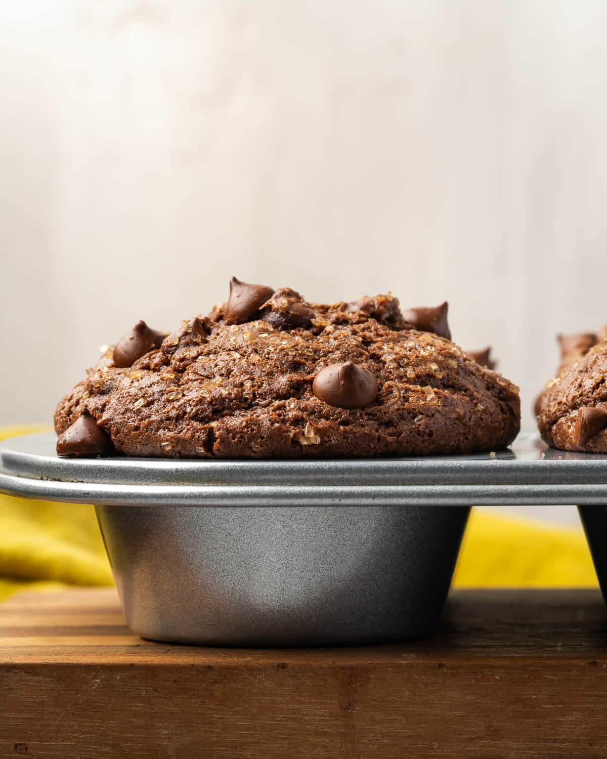 Freshly baked gluten free chocolate muffins in a muffin tin sitting on a wooden cutting board.