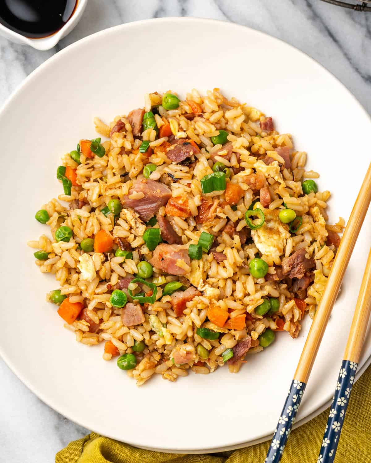 A serving dish filled with ham fried rice sitting next to chop sticks. 