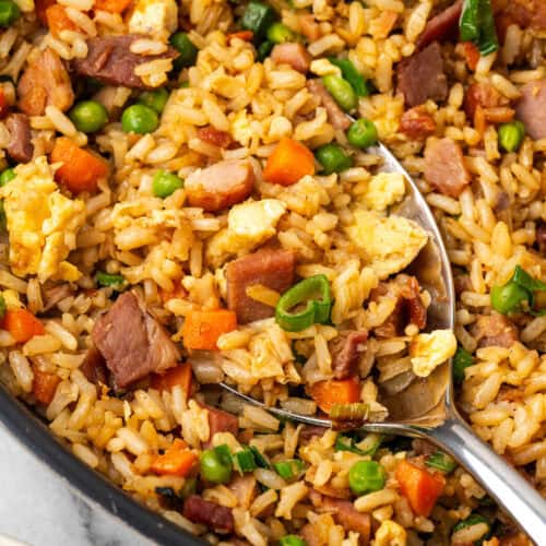 A serving spoon scooping ham fried rice from a skillet.