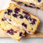 A loaf of lemon blueberry pound cake cut into slices and sitting on a wooden cutting board.
