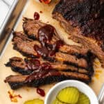 Several slices of BBQ brisket topped with BBQ sauce sitting on a metal tray.
