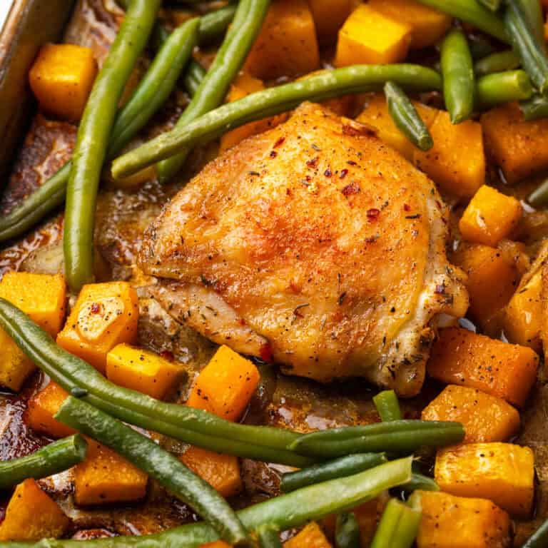 Baked chicken thighs with squash and green beans on a sheet pan.