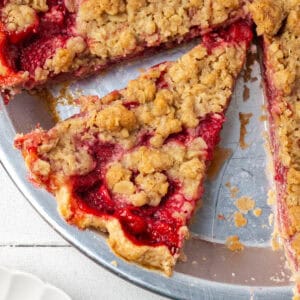 A slice of strawberry crumble pie sitting in a metal pie tin.
