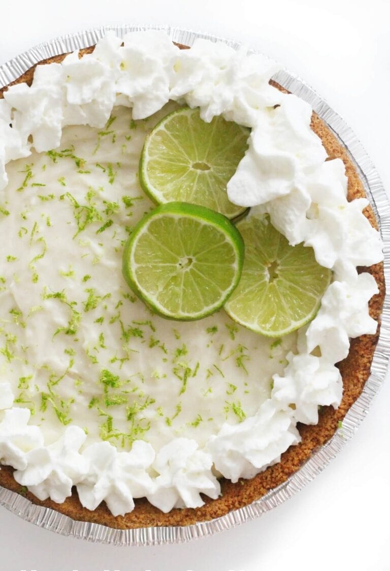 A no bake key lime pie topped with whipped cream and lime slices.