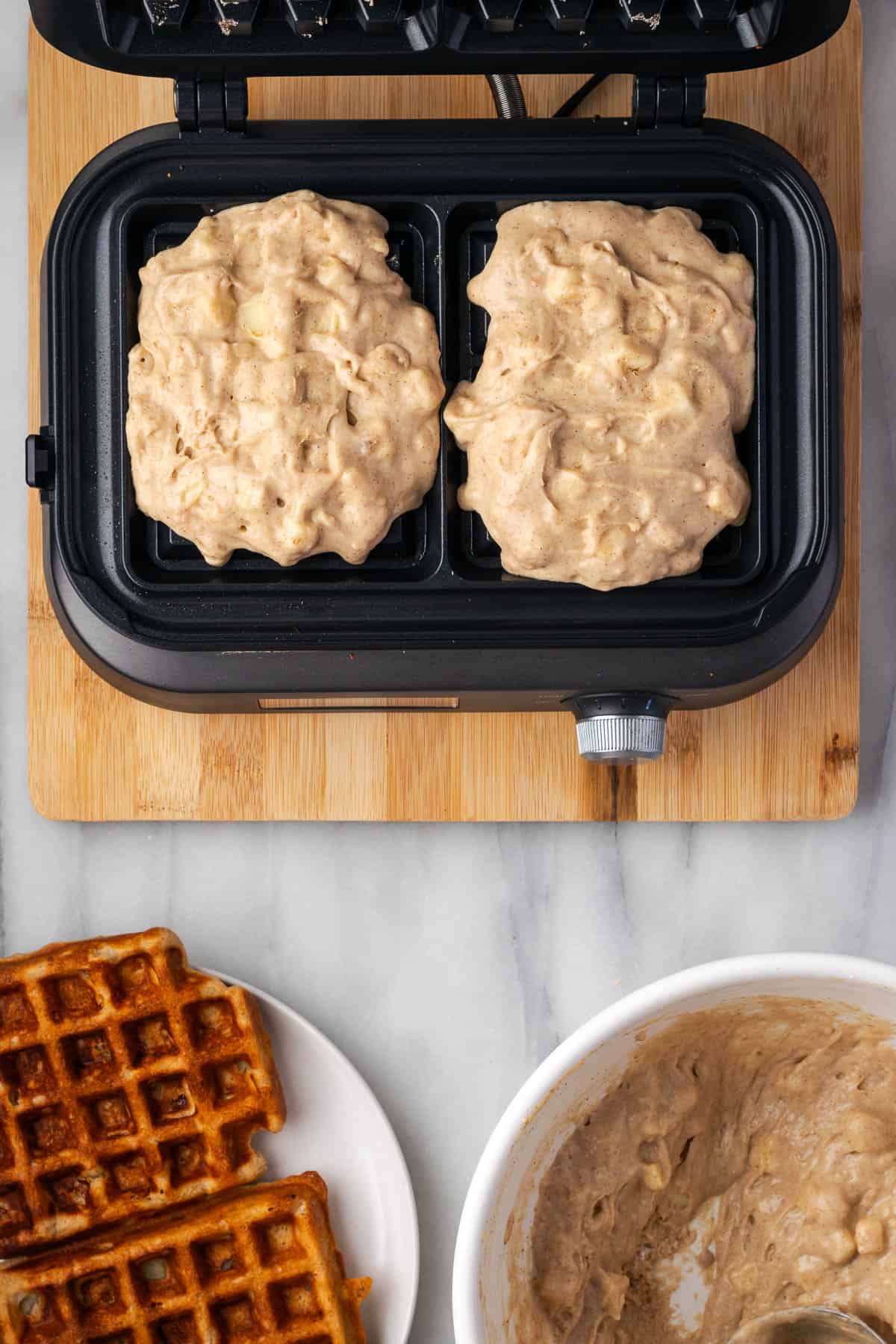 Waffle batter being added to a waffle iron for cooking. 