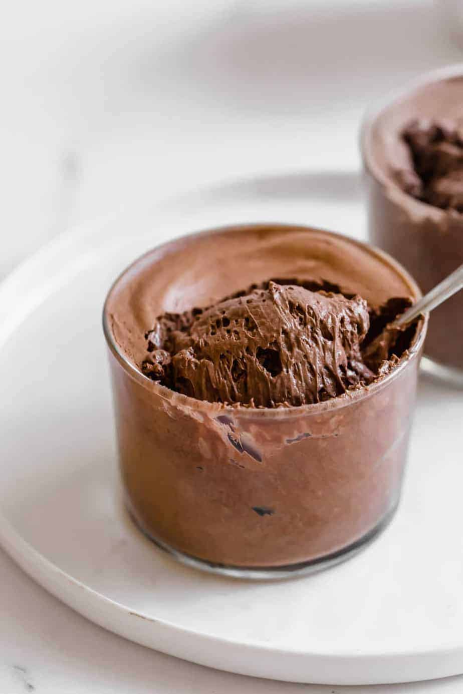 A spoon scooping chocolate mousse from a small glass dish.