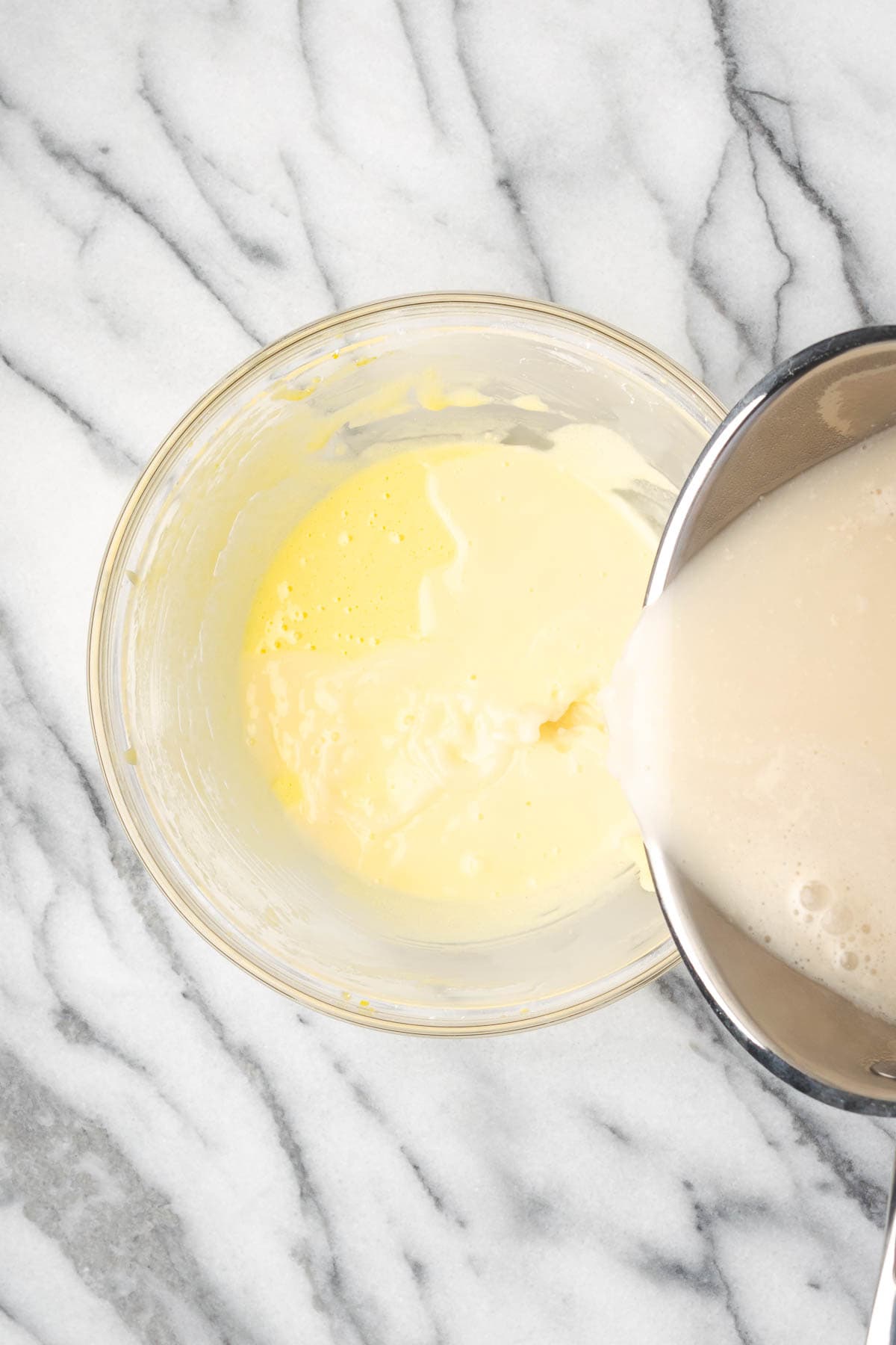 Hot milk being slowly added to the egg yolk mixture.