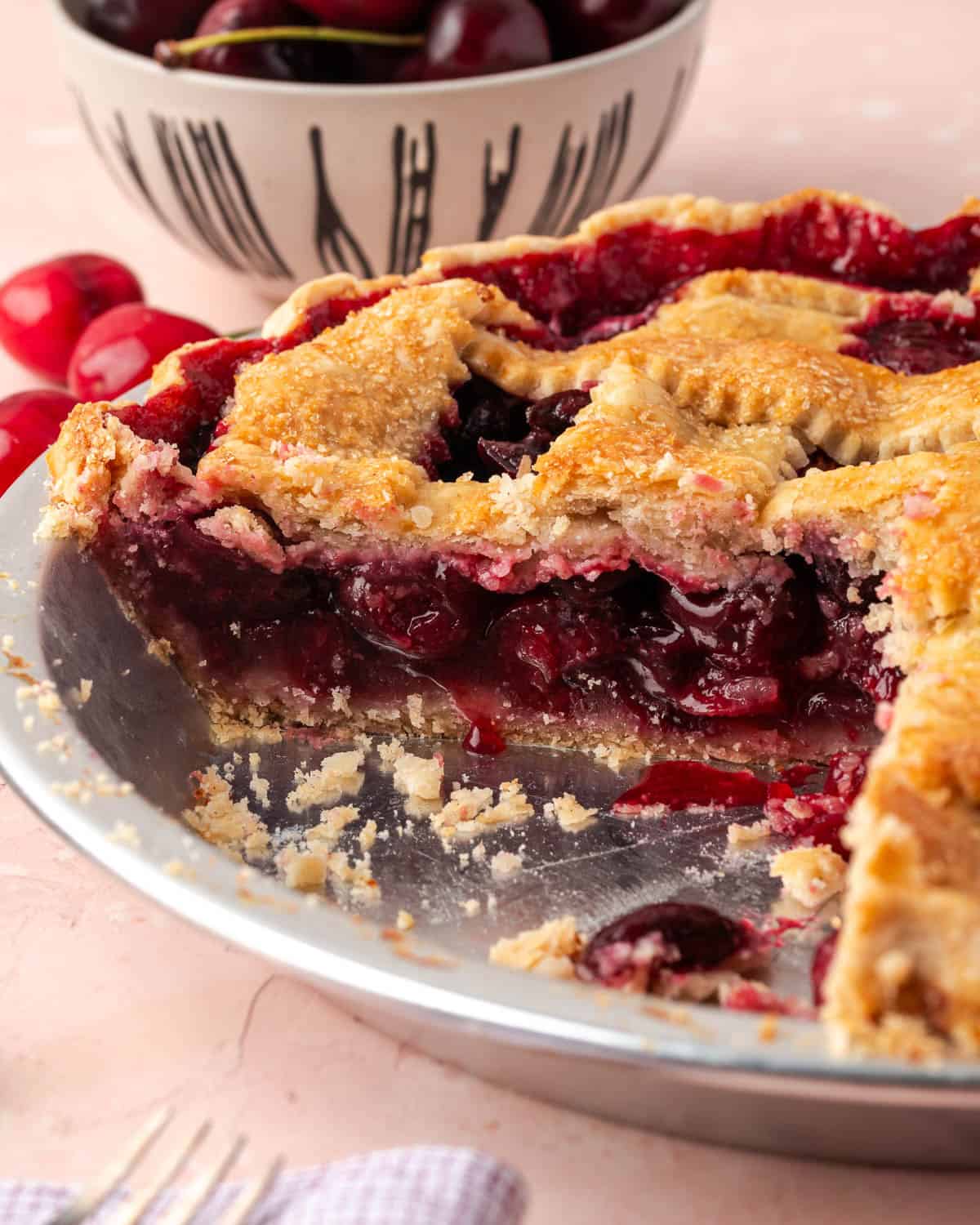 A sliced gluten free cherry pie in a metal pie plate showing the filling inside. 