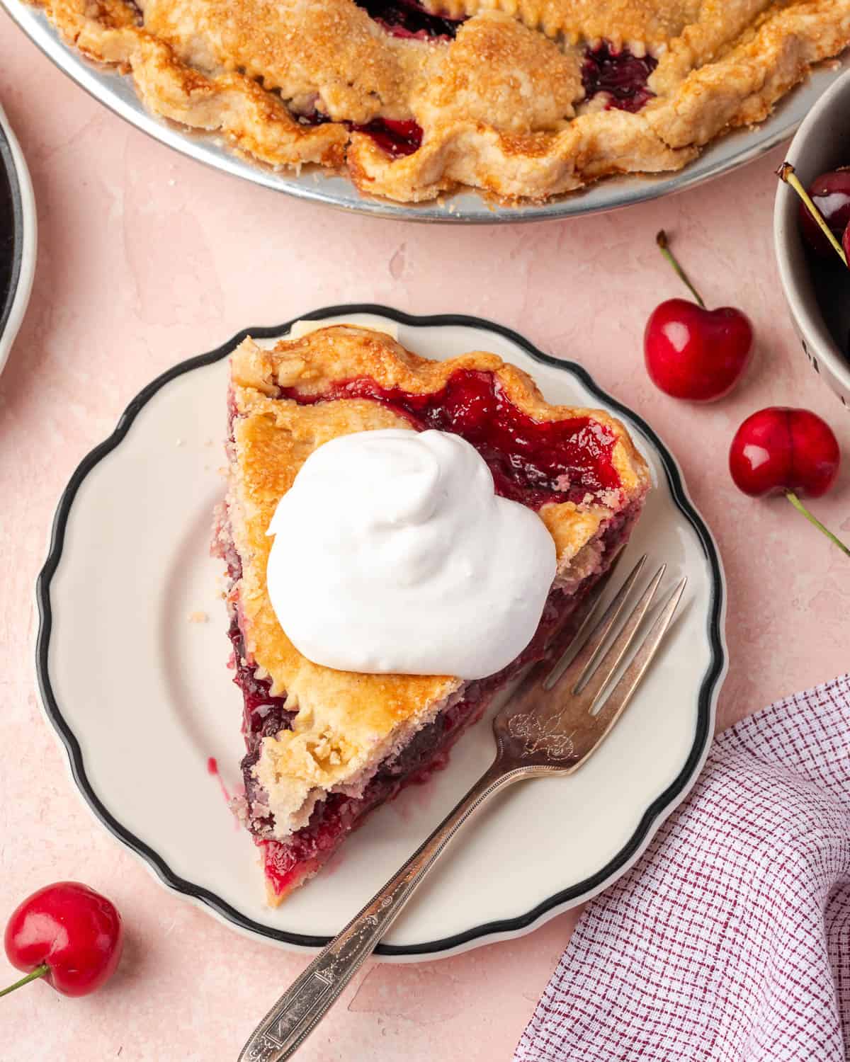A slice of gluten free cherry pie topped with whipped cream served on a small dessert plate.