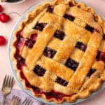 A gluten free cherry pie sitting on a table next to a bowl of fresh cherries.