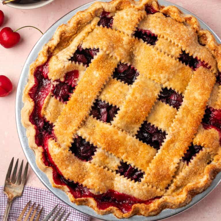 A gluten free cherry pie sitting on a table next to a bowl of fresh cherries.