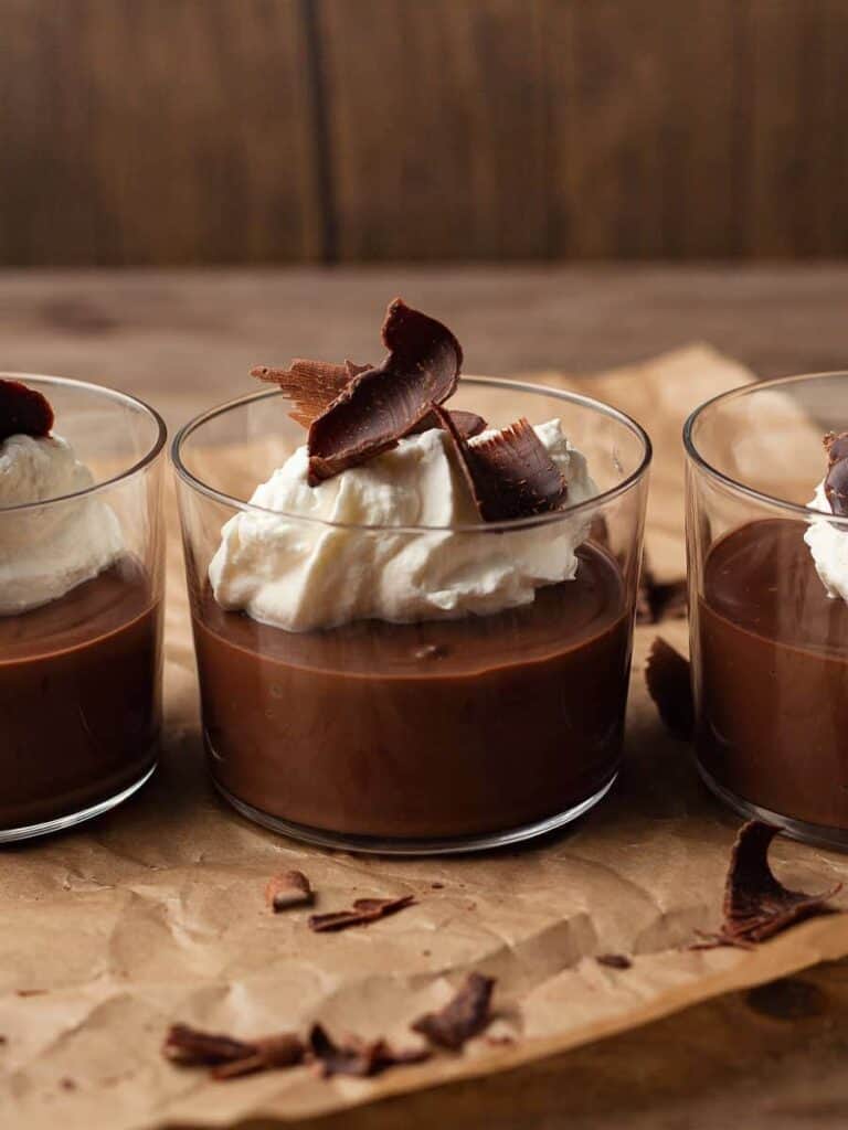 Single servings of gluten free chocolate pudding topped with whipped cream and shaved chocolate.