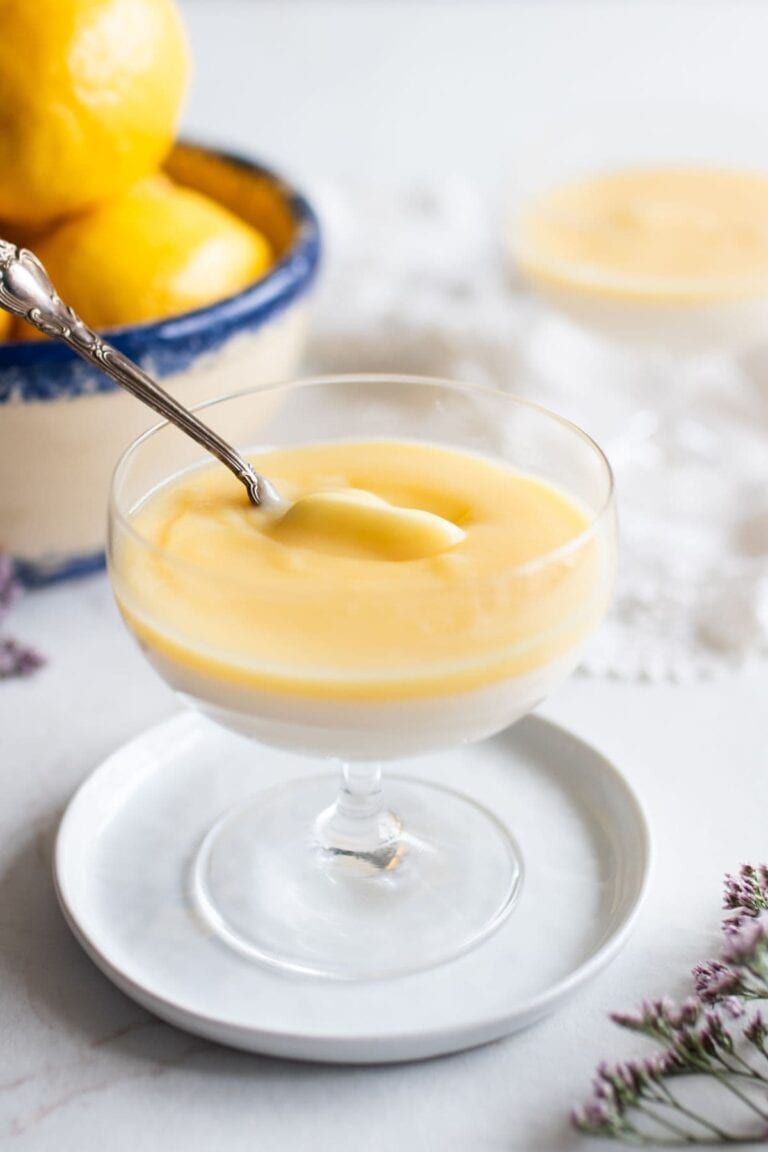 A spoon taking a scoop of lemon panna cotta from a fancy serving glass.