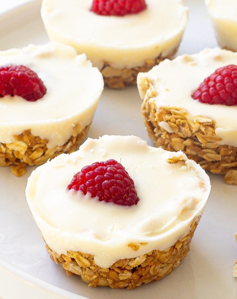 Several oat cups topped with white chocolate and fresh raspberries sitting on a tray.