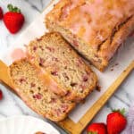 A sliced loaf of strawberry banana bread sitting on a cutting board.