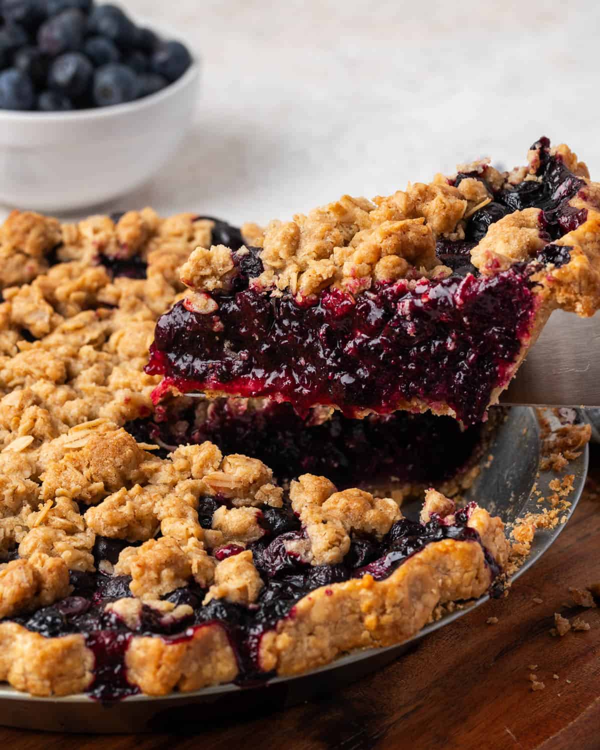 A slice of blueberry crumble pie being lifted from a pie plate.
