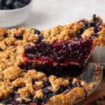 A slice of blueberry crumble pie being lifted from a pie pan.