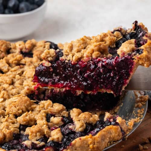 A slice of blueberry crumble pie being lifted from a pie pan.