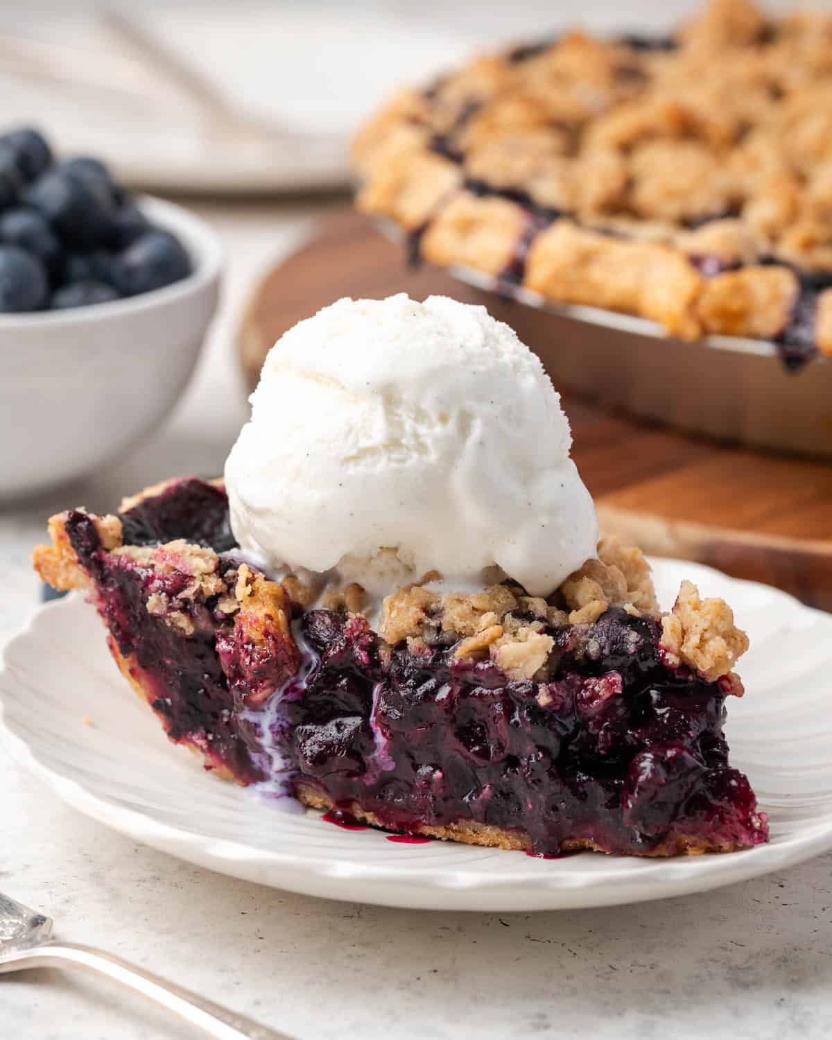 A slice of blueberry pie topped with vanilla ice cream sitting on a small dessert plate.